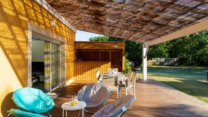 Un patio techado con suelo de madera, una parrilla y mobiliario exterior que incluye dos sillas y una mesa.