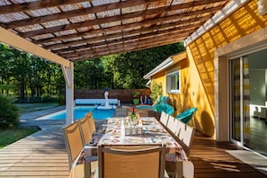 An outdoor patio with a pool, dining table, and chairs.