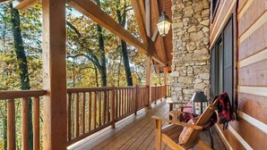 A wooden deck with a stone wall and a window, overlooking a forest. - Cinnamon Valley - The Elk Lodge (Eureka Springs)