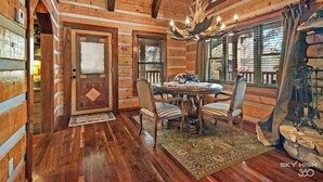 A wooden cabin interior with a round dining table, four chairs, a chandelier, and a stone fireplace. - Cinnamon Valley - The Elk Lodge (Eureka Springs)