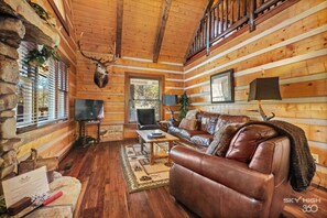 A log cabin interior with a leather sofa, a television, and a deer head mounted on the wall. - Cinnamon Valley - The Elk Lodge (Eureka Springs)