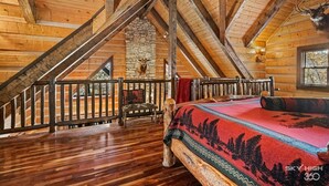 A log cabin with a wooden interior, a stone wall, a bed with a red blanket, and a mounted deer head. - Cinnamon Valley - The Elk Lodge (Eureka Springs)