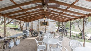 An outdoor covered patio with a ceiling fan, white plastic chairs, and tables.