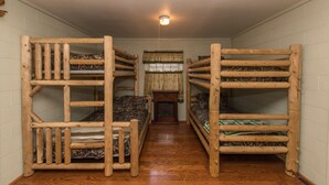 A room with bunk beds arranged in a central aisle, wooden walls, and a ceiling light fixture.