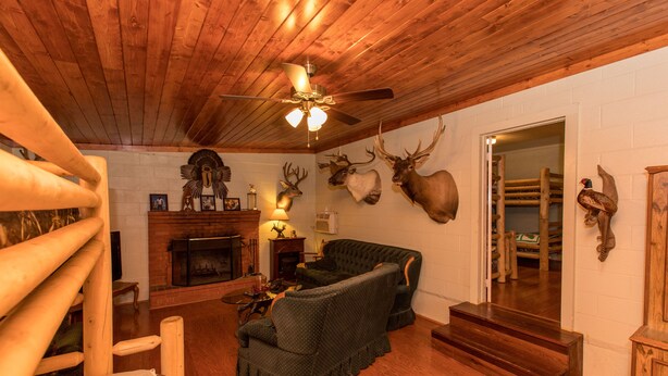 A cozy log cabin interior with a fireplace, wooden furniture, and mounted animal heads on the wall.