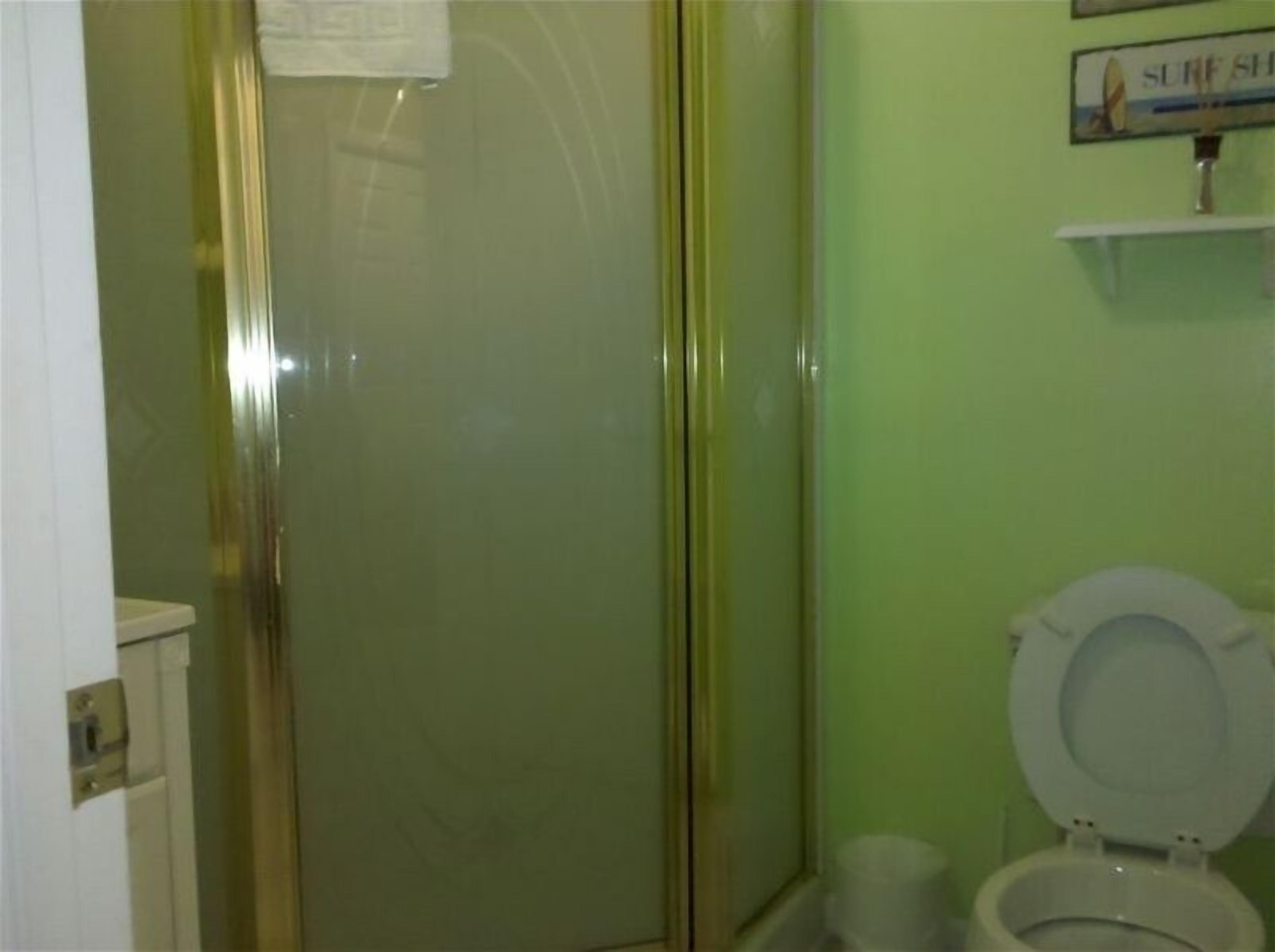 Une salle de bain avec une douche à parois de verre, des toilettes blanches et un panneau placé au-dessus des toilettes.