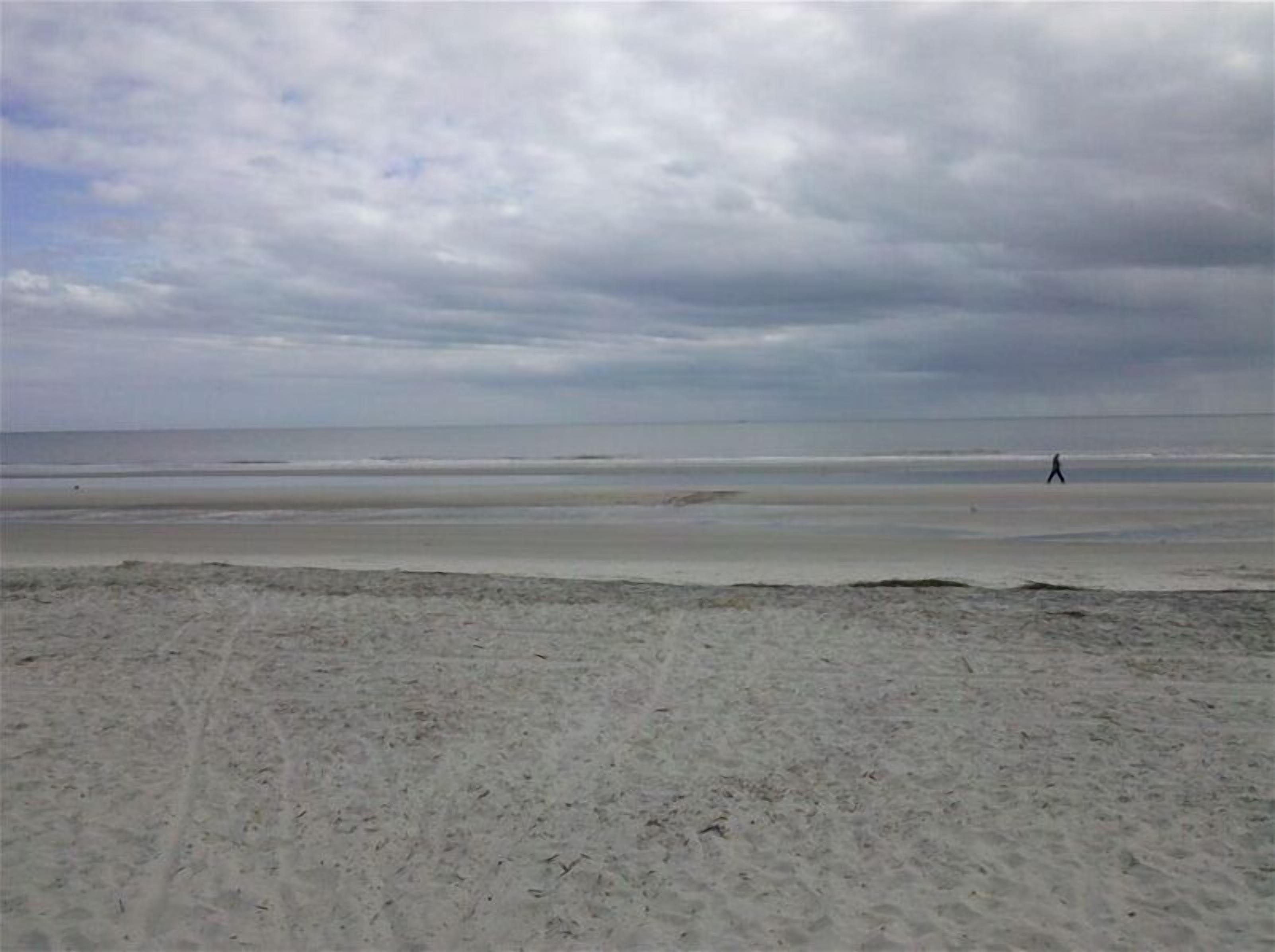 A beach with a wide sandy area and a person walking in the distance.