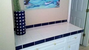 A bathroom with a tiled countertop, a decorative vase, and a painting of a beach scene. - 338 Ocean View!  Quiet Villa W/ Many Amenities 550 Sq FeetVRBO#394687 (Hilton Head Island)