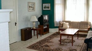 A living room with a fireplace, a television, a sofa, and a coffee table. - Beautiful 1921 brick and fieldstone Country Country ... The Tummel house (Roblin)