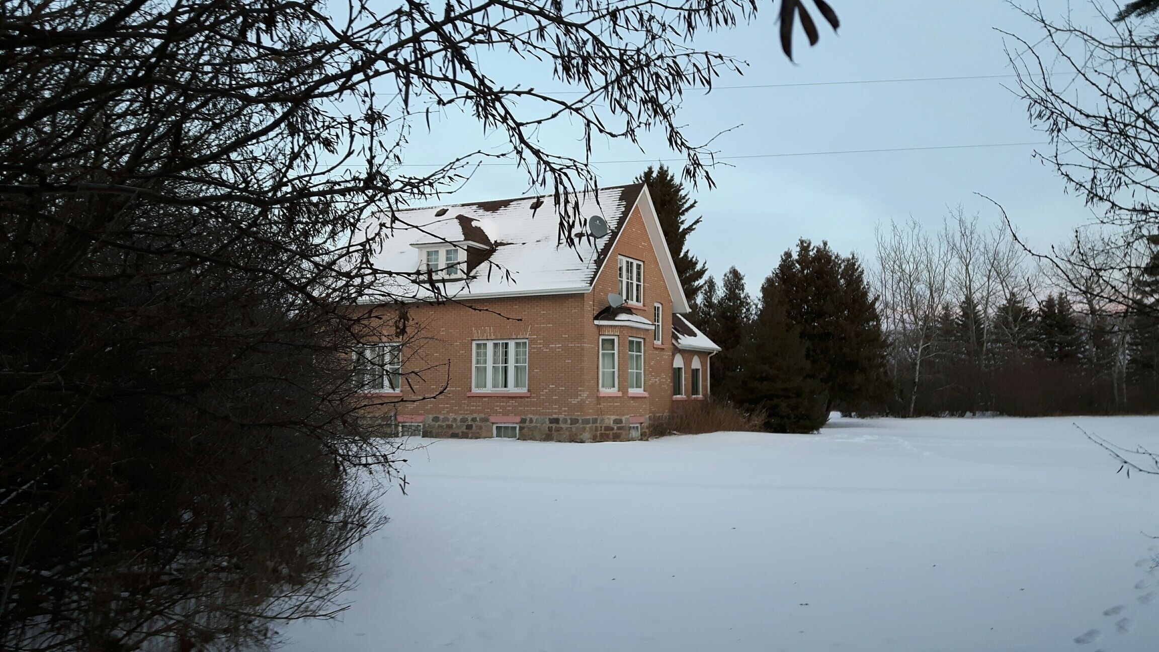 A two-story house with a steeply pitched roof, brick exterior, and a snow-covered yard.