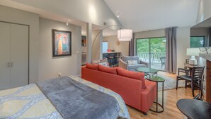 Une chambre d’hôtel moderne avec un lit, un canapé rouge, une petite table à manger et un balcon avec vue.