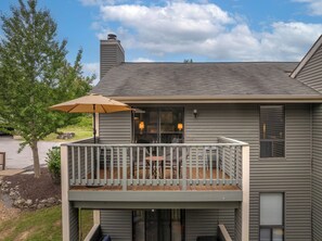 A two-story house with a balcony, a patio with outdoor furniture, and a large window.