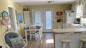 Un salon chaleureux avec un coin repas, un plancher en bois et une cuisine dotée de meubles blancs.
