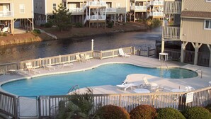 Une piscine privée dotée de chaises longues et d’une terrasse en bois, le tout entouré d’une clôture et agrémenté d’un aménagement paysager.