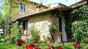 A stone building with a tiled roof, surrounded by lush greenery and flowering plants.