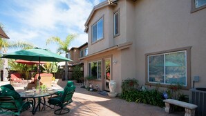 A patio with a table and chairs, a green umbrella, and a stone bench. - Carlsbad treasure in Calavera Hills (carlsbad)
