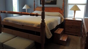A bedroom with a wooden four-poster bed, a nightstand with a lamp, a dresser, and a window with blinds. - Carlsbad treasure in Calavera Hills (carlsbad)