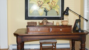 Een houten bureau met een lamp, een lijst met foto en een rieten mand.