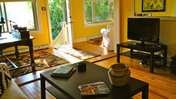 Een woonkamer met houten vloer, een bank, een salontafel, een televisie en een boekenplank.