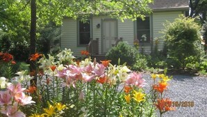 Een huis met een veranda, omringd door een tuin vol verschillende bloemen.