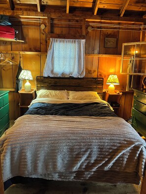 Un dormitorio estilo cabaña de madera con una cama, dos lámparas de noche, una lámpara colgante y un cabecero de madera.