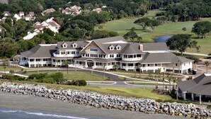 A large, multi-story residential building with a prominent porch area, situated near a rocky shoreline. - PRISTINE BEACH, GOLF, TENNIS!  BEAUTIFUL AND SPACIOUS 2BR COURTSIDE VILLA!  (Seabrook Island)