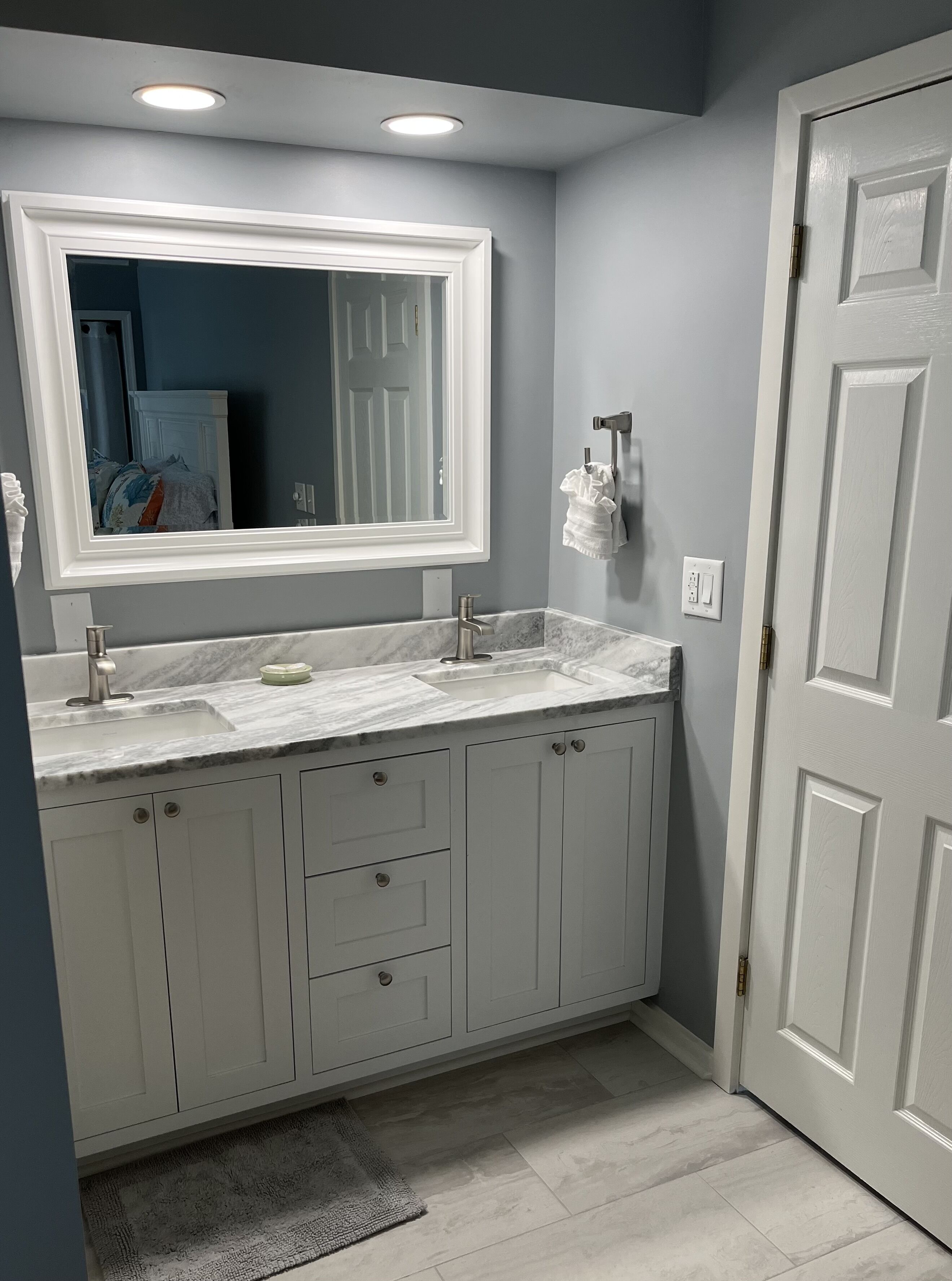 Une salle de bain avec un meuble-lavabo blanc, un grand miroir et une porte blanche.