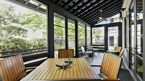 A covered outdoor seating area with wooden tables and chairs, large windows, and a ceiling fan.