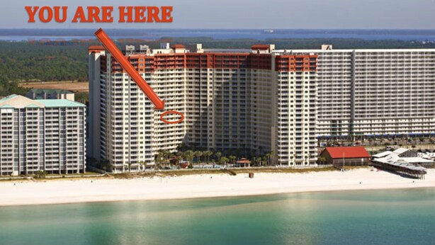 A large hotel with multiple floors, a beach in the foreground, and a body of water in the background.