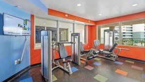 A gym with exercise equipment, a TV screen, and large windows.