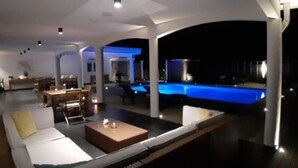 A modern interior with a pool area, featuring a seating area with a table and chairs, and a pool with blue lighting.