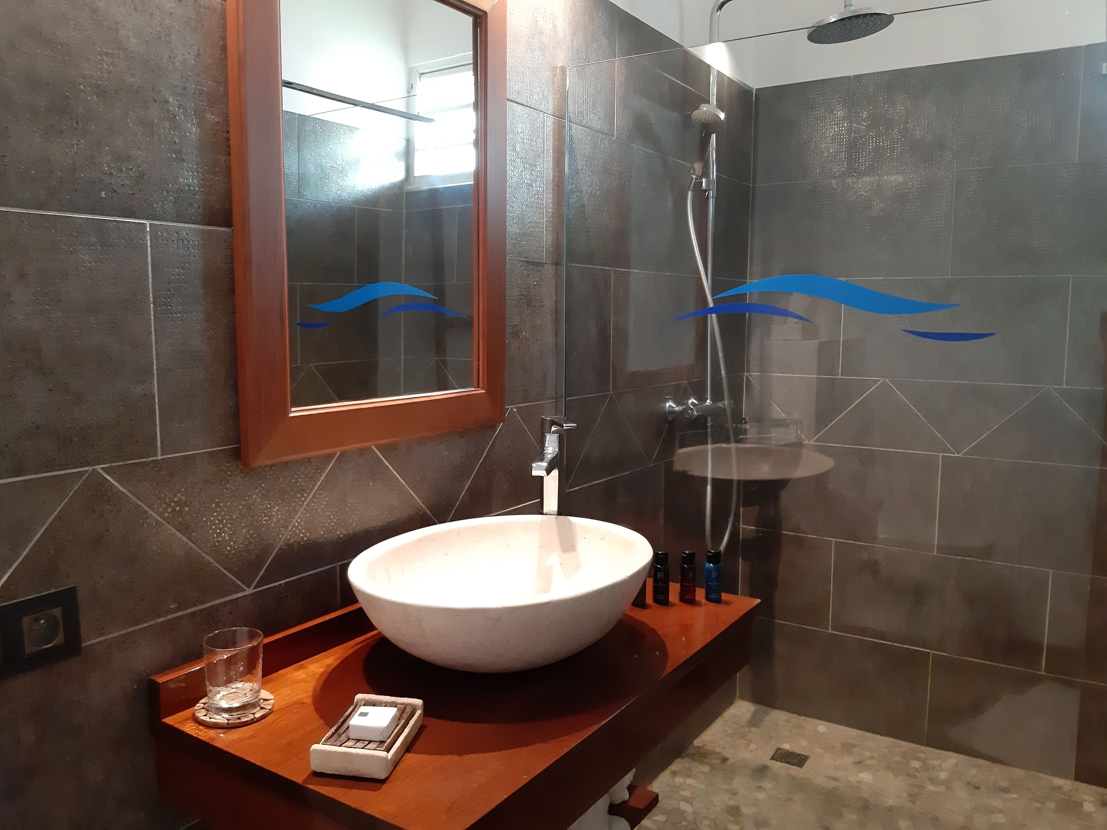 A bathroom with a large white vessel sink, a handheld showerhead, and a mirror with a blue wave design.