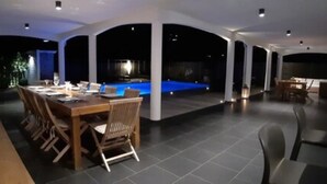 A spacious indoor area with a pool, a dining table with chairs, and a seating area with a lamp.
