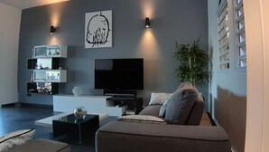 A modern living room with a flat-screen TV, a sofa, a coffee table, and decorative shelves.
