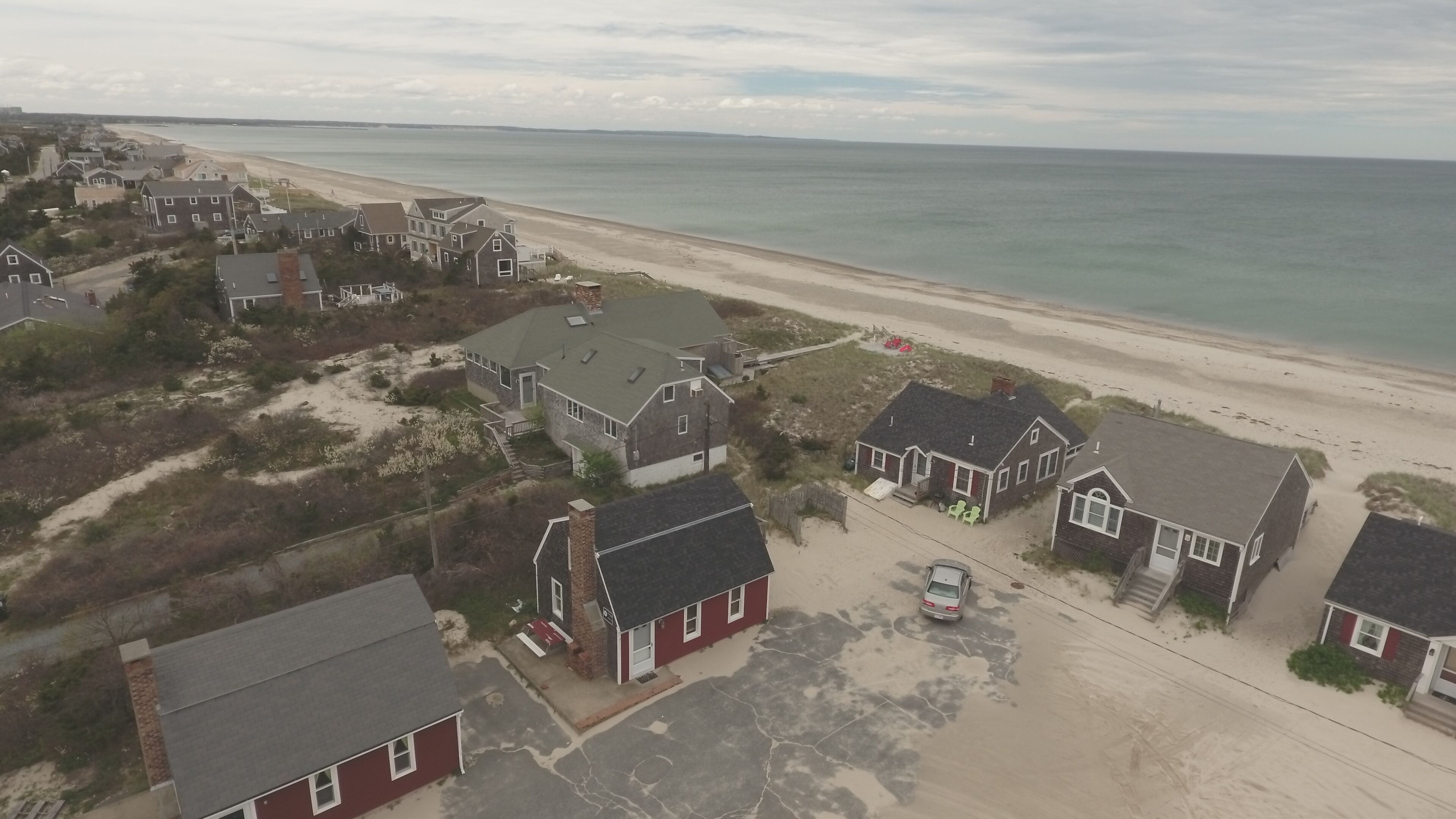 An aerial view of a coastal residential area with houses, a beach, and a clear sky.