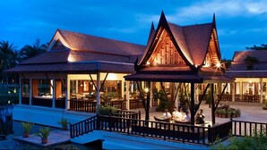A traditional Thai-style building with a covered walkway and a pond in the foreground. - Beachfront condo with full sea view and the facilities of a 5-star resort (Petchaburi)