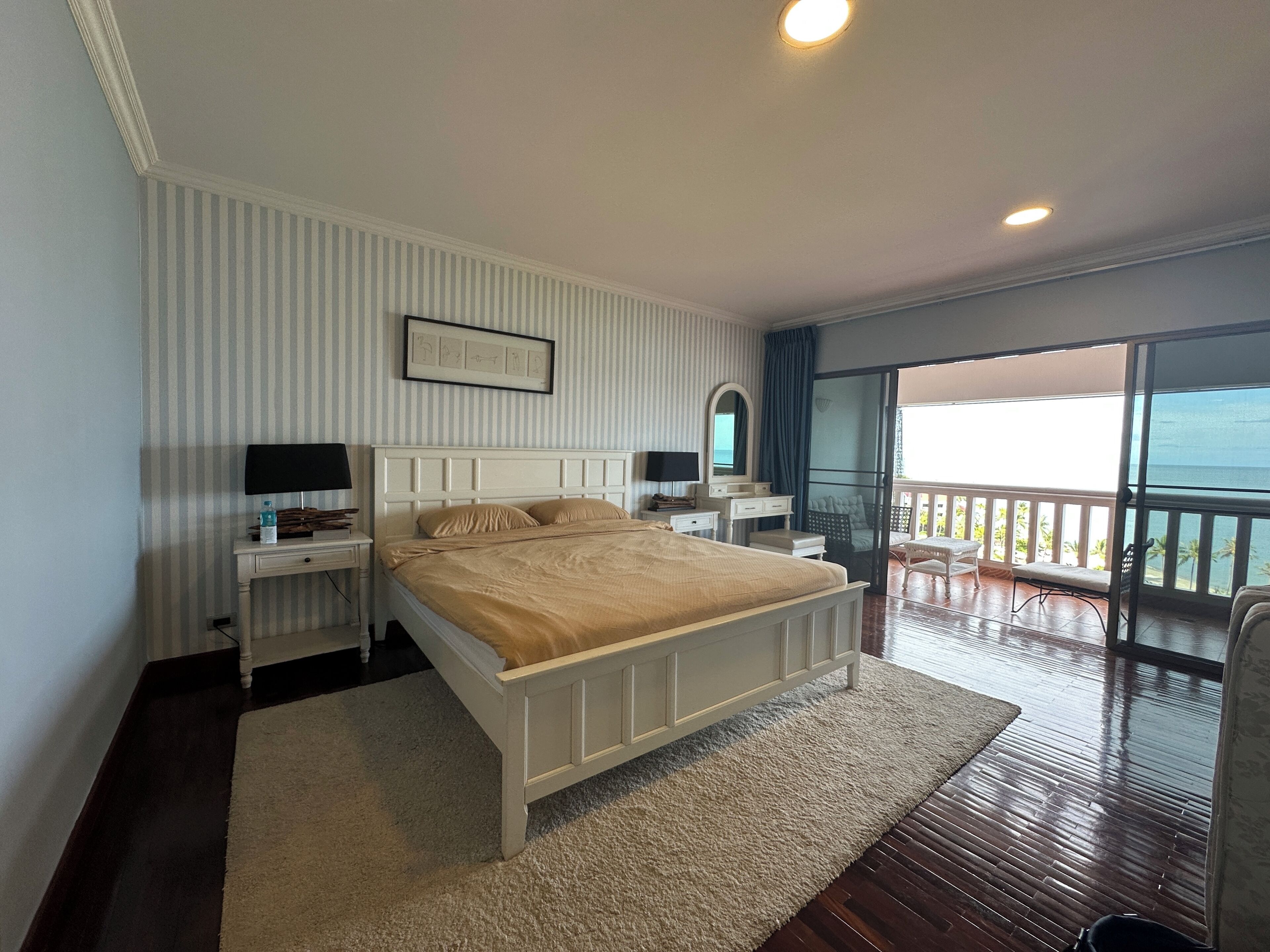Une chambre à coucher avec un lit, des tables de chevet, un miroir et une vue sur l’océan.