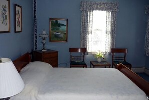A bedroom with a bed, a nightstand, a lamp, a chair, a small table with a vase, and a painting on the wall. - Ocean front house with two private beaches-- on a peninsula--spectacular views! (Milbridge)