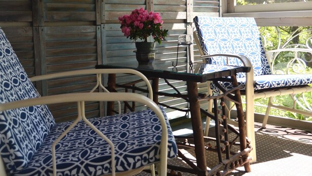 A covered porch with wicker furniture, a table with a vase of flowers, and a hanging lantern. - Quiet, peaceful, great central location.  Come visit! (Mt. Desert)