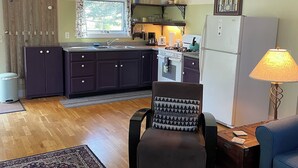 A compact kitchen with a central island, a dining area with a blue sofa, and a patterned rug. - Quiet, peaceful, great central location.  Come visit! (Mt. Desert)
