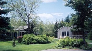 A small, single-story house with a front porch, surrounded by a well-maintained lawn and various shrubs. - Quiet, peaceful, great central location.  Come visit! (Mt. Desert)