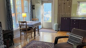 A living room with a dining table, chairs, a sofa, a rug, and a kitchen area with cabinets. - Quiet, peaceful, great central location.  Come visit! (Mt. Desert)