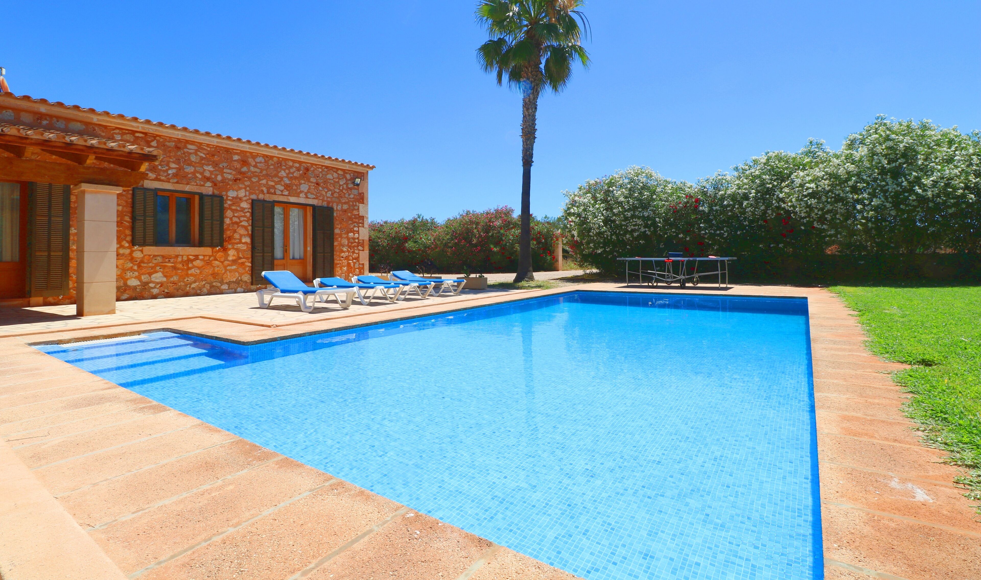 A swimming pool with lounge chairs and a table, surrounded by a stone building and greenery.