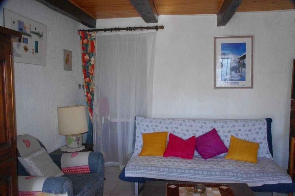 A cozy room with a patterned sofa, a chair with cushions, a lamp, and a framed picture on the wall.