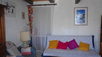 A cozy room with a patterned sofa, a chair with cushions, a lamp, and a framed picture on the wall.