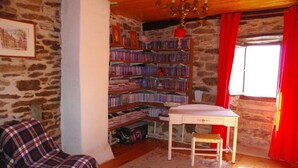 Une pièce chaleureuse avec un mur en pierre, une bibliothèque remplie de livres, un petit bureau, une chaise et une fenêtre ornée de rideaux rouges.