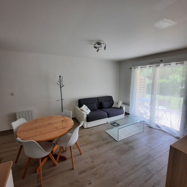 A modern living room with a round wooden table, white chairs, a dark sofa, and a glass coffee table. - Apartment/ flat - Pleneuf val andre (Pléneuf-Val-André)