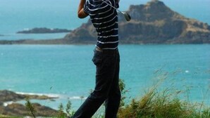 A person playing golf on a green with a scenic ocean view in the background.