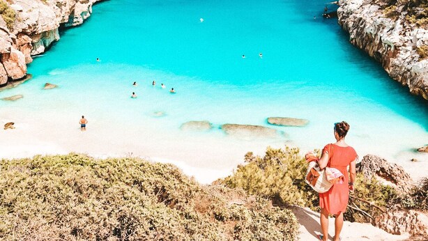Een kustlandschap met helder turquoise water, rotsachtige kliffen en schaarse begroeiing.