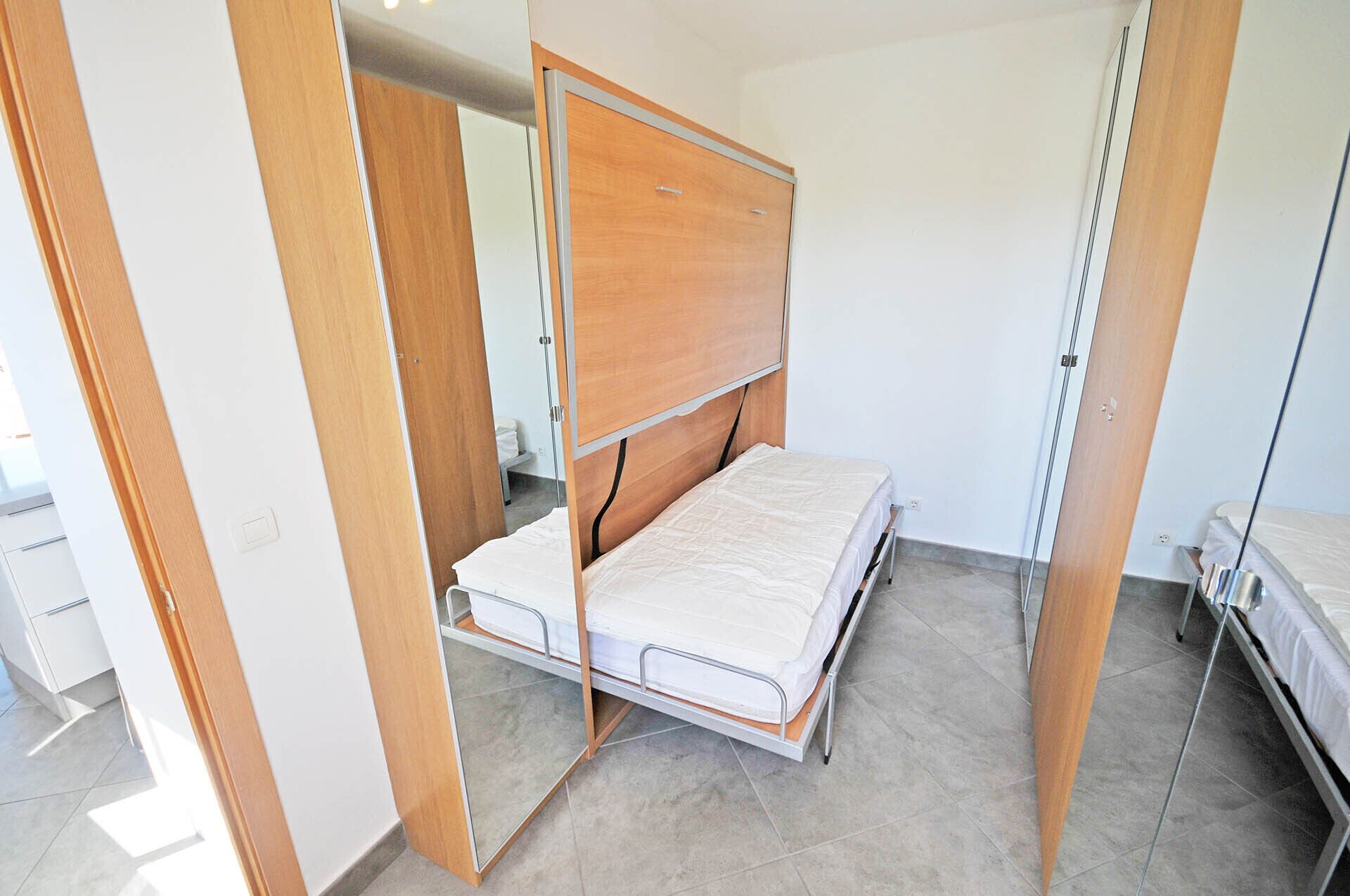 A bedroom with a bed, wooden wardrobe, and a mirror.